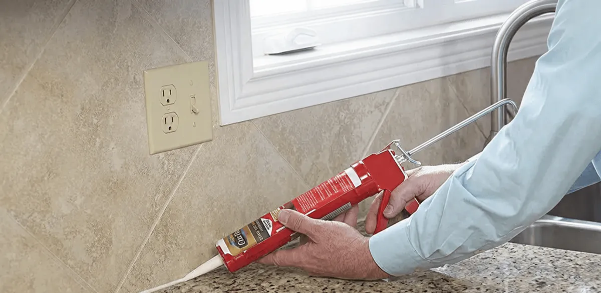 Handyman applying caulk along a kitchen backsplash and countertop seam in Kansas City, MO